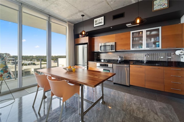 kitchen with backsplash, stainless steel appliances, sink, decorative light fixtures, and a wall of windows