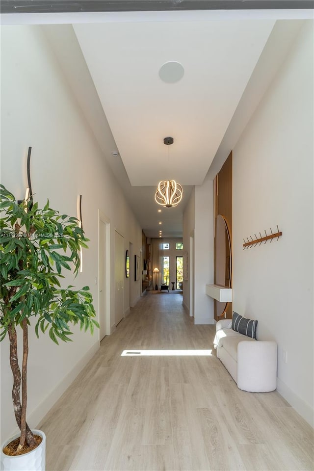 hallway featuring baseboards, light wood finished floors, and a notable chandelier