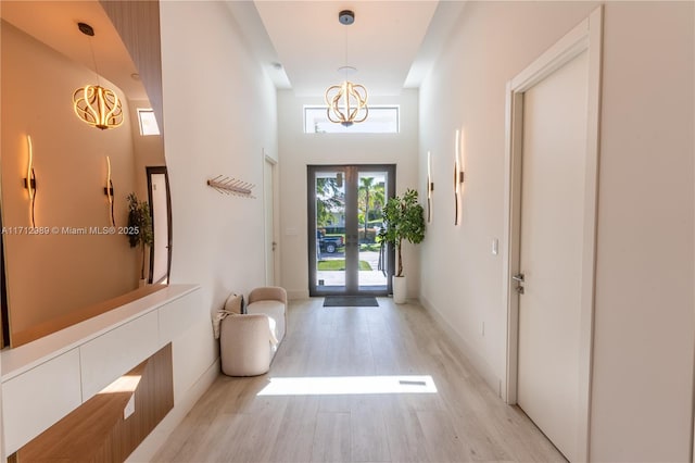 doorway to outside featuring baseboards, french doors, a high ceiling, and light wood-style floors