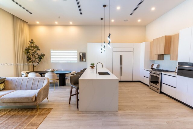 kitchen with sink, white cabinetry, hanging light fixtures, a kitchen island with sink, and high end appliances