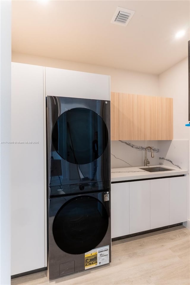 laundry room featuring sink, light hardwood / wood-style floors, cabinets, and stacked washing maching and dryer