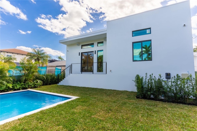 back of property with a yard, an outdoor pool, fence, and stucco siding