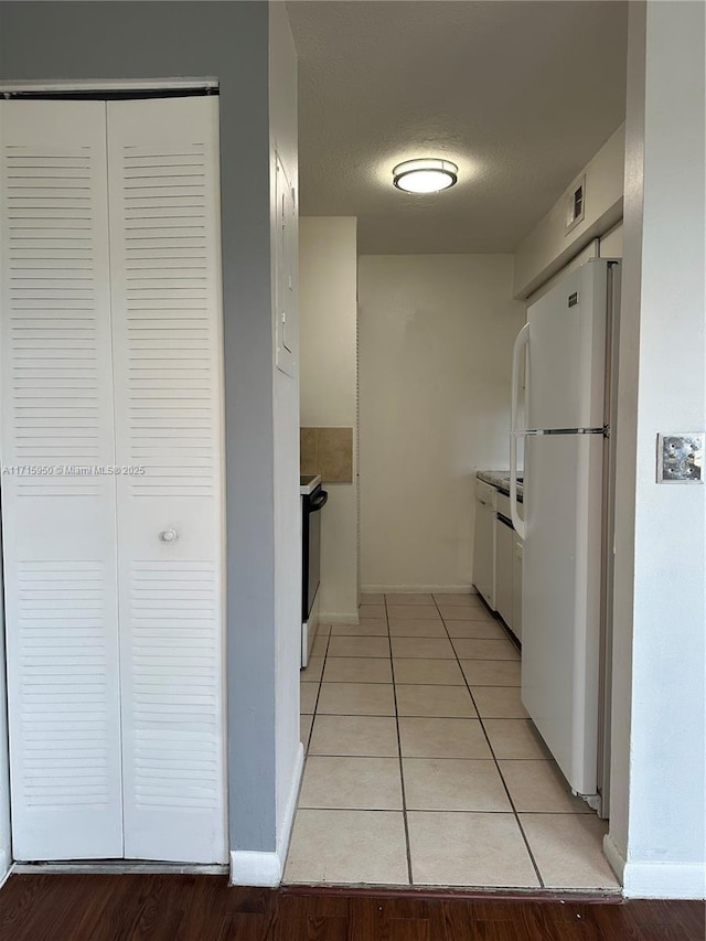 kitchen with white cabinets, white refrigerator, light tile patterned floors, and a textured ceiling