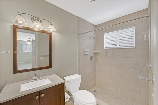 bathroom featuring ceiling fan, toilet, a tile shower, and vanity