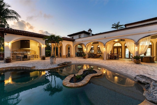 back of property at dusk with a patio area, an outdoor pool, and stucco siding