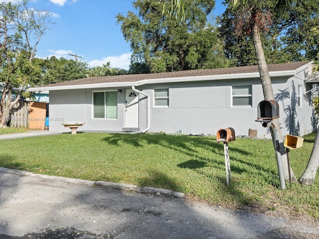 ranch-style home featuring a front lawn, fence, brick siding, and stucco siding