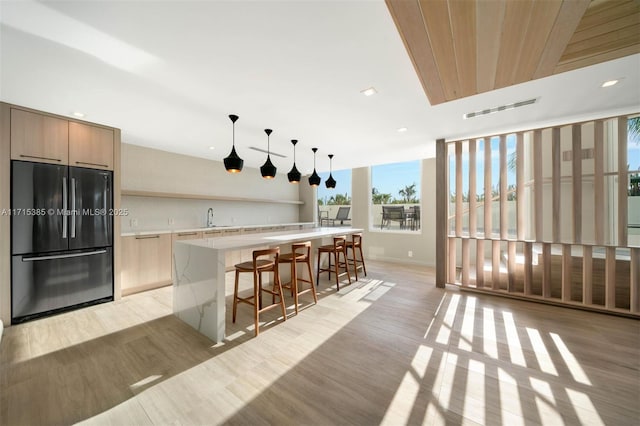 kitchen featuring sink, hanging light fixtures, a kitchen breakfast bar, stainless steel fridge, and light wood-type flooring