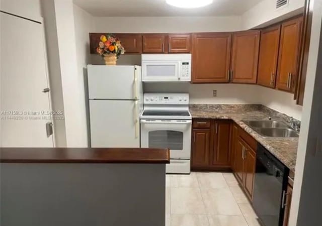 kitchen with light tile patterned flooring, white appliances, dark stone countertops, and sink