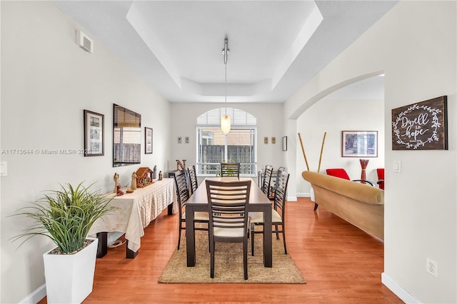 dining space featuring a tray ceiling, wood finished floors, visible vents, arched walkways, and baseboards