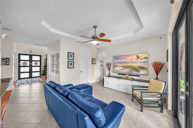 living room featuring french doors, a tray ceiling, ceiling fan, and light tile patterned flooring