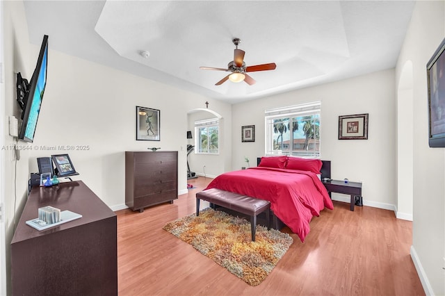 bedroom featuring arched walkways, light wood-type flooring, baseboards, and ceiling fan