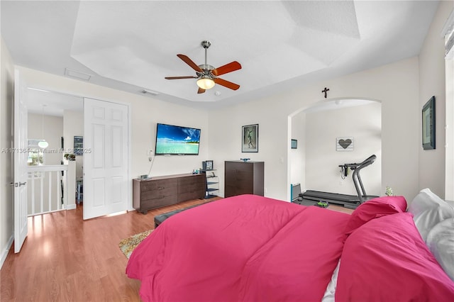 bedroom featuring arched walkways, visible vents, wood finished floors, ceiling fan, and a raised ceiling