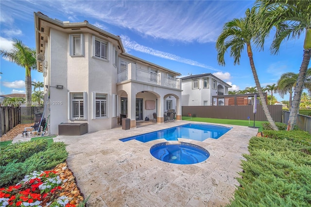 rear view of property with a fenced backyard, a balcony, stucco siding, an in ground hot tub, and a patio