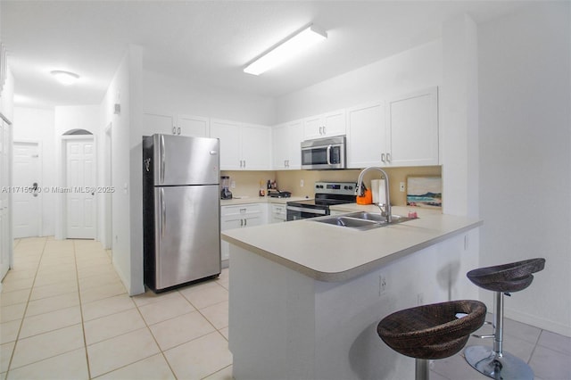 kitchen with kitchen peninsula, a kitchen breakfast bar, stainless steel appliances, white cabinetry, and light tile patterned flooring