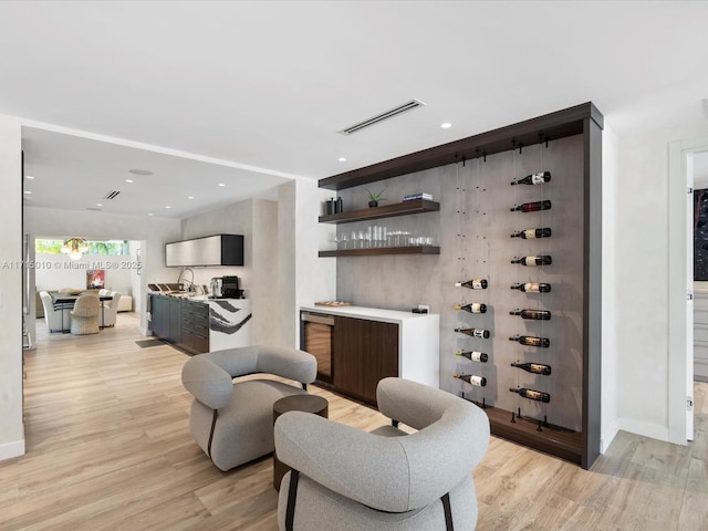 interior space featuring beverage cooler, light hardwood / wood-style floors, and wet bar