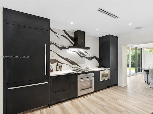 kitchen with cooktop, range hood, paneled built in refrigerator, oven, and light hardwood / wood-style floors