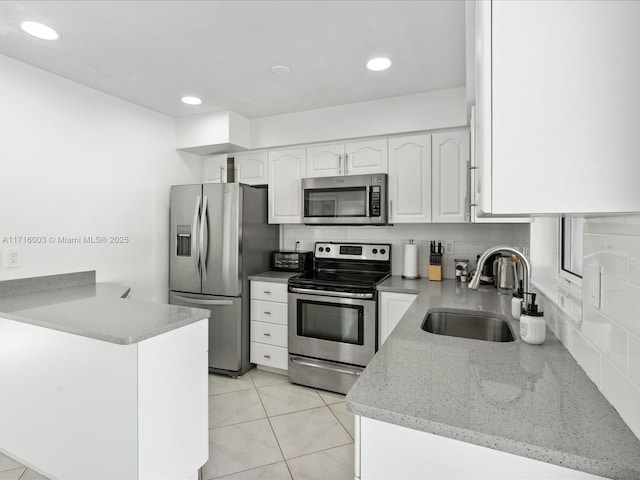 kitchen with appliances with stainless steel finishes, white cabinetry, sink, light stone counters, and kitchen peninsula