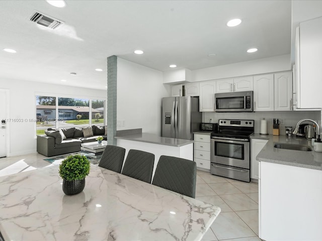 kitchen featuring sink, white cabinetry, light tile patterned floors, appliances with stainless steel finishes, and a kitchen breakfast bar