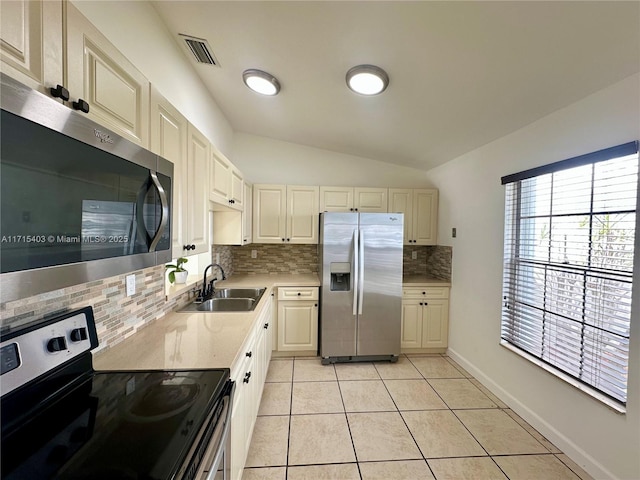 kitchen featuring vaulted ceiling, light tile patterned flooring, appliances with stainless steel finishes, sink, and backsplash