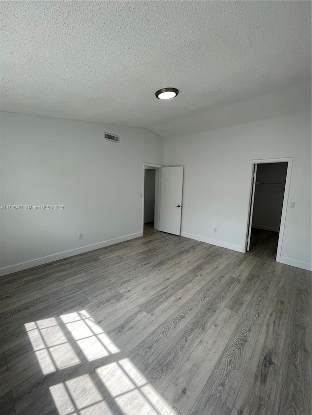 empty room with wood-type flooring, a textured ceiling, and vaulted ceiling