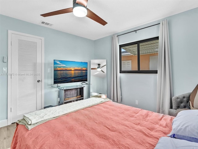 bedroom featuring a fireplace, light hardwood / wood-style flooring, and ceiling fan