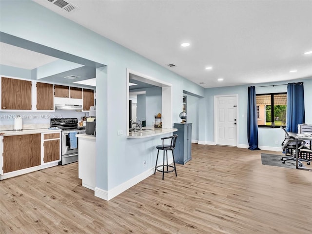 kitchen with sink, light hardwood / wood-style flooring, kitchen peninsula, stainless steel electric range, and a breakfast bar