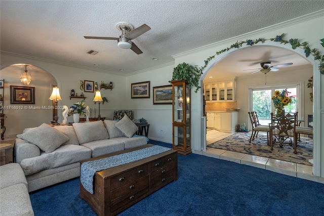 tiled living room featuring ceiling fan, ornamental molding, and a textured ceiling