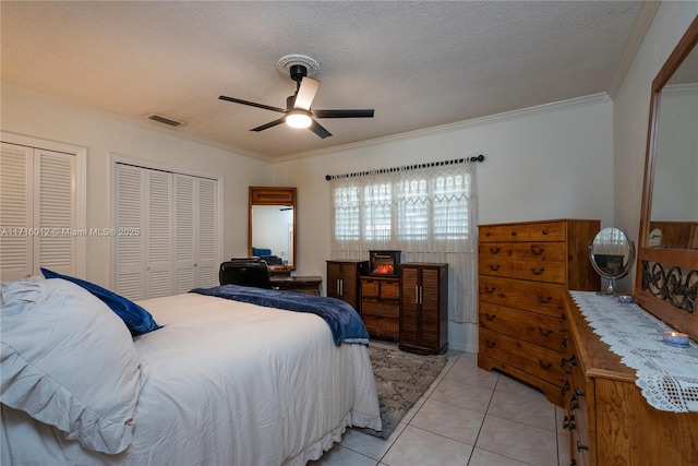 tiled bedroom featuring ceiling fan, ornamental molding, a textured ceiling, and two closets