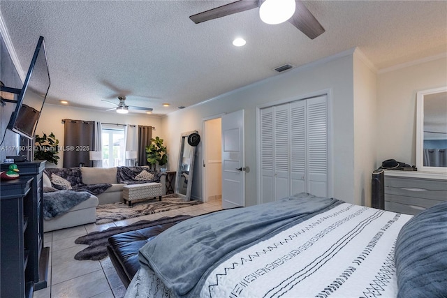 bedroom with a textured ceiling, ceiling fan, crown molding, light tile patterned floors, and a closet