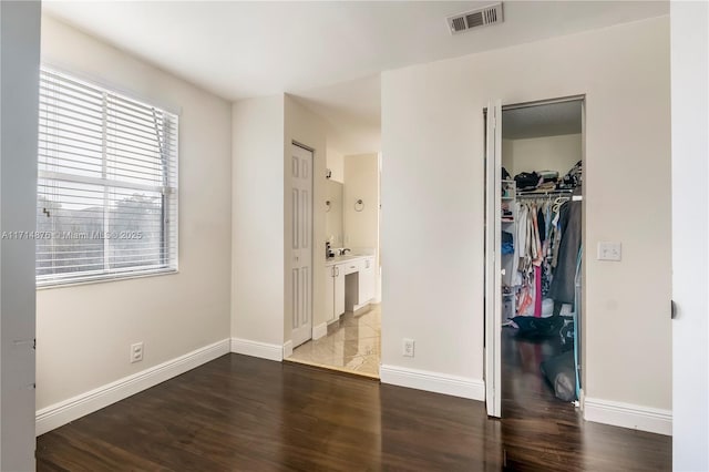 unfurnished bedroom with wood finished floors, visible vents, a spacious closet, and baseboards
