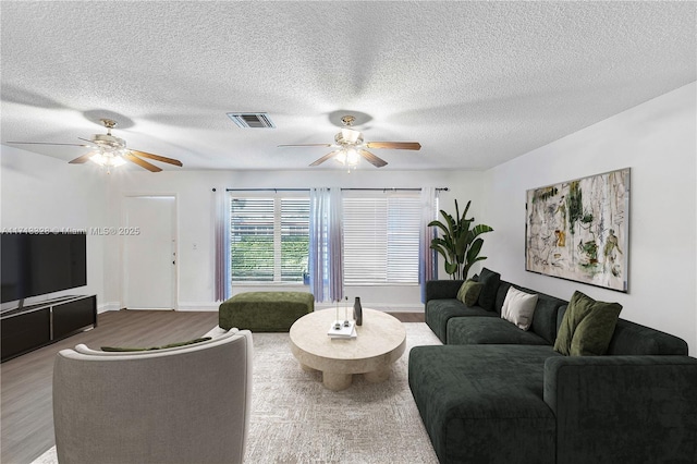 living room with a ceiling fan, wood finished floors, visible vents, and a textured ceiling