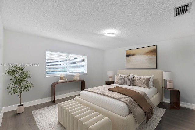 bedroom with visible vents, a textured ceiling, baseboards, and wood finished floors