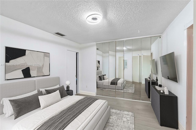 bedroom featuring visible vents, a textured ceiling, and light wood finished floors