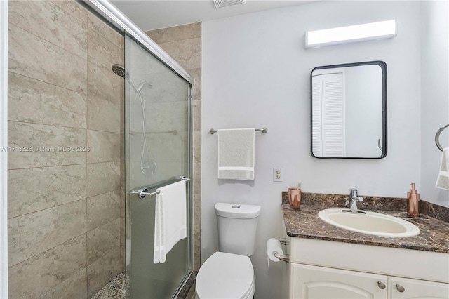 bathroom with vanity, a shower stall, toilet, and visible vents