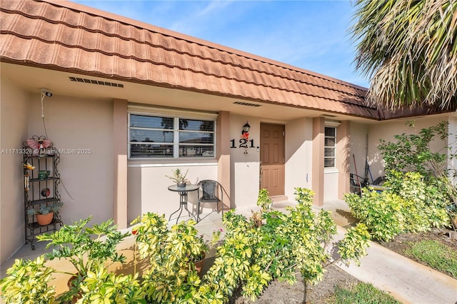 property entrance with stucco siding, visible vents, and a tiled roof