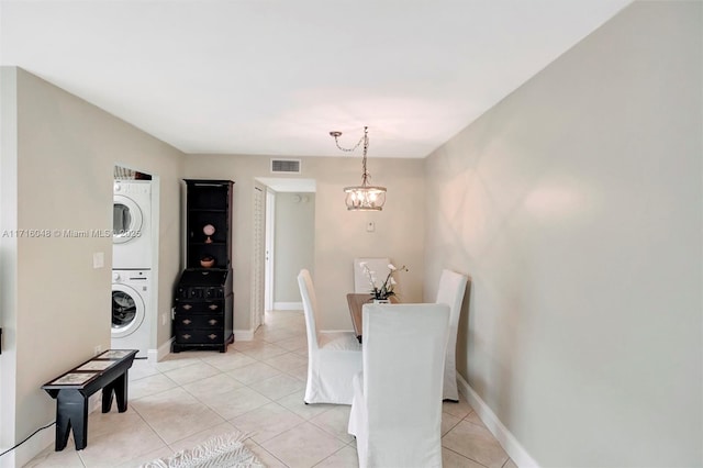 tiled dining area with stacked washer / drying machine and an inviting chandelier