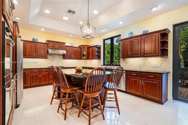 kitchen featuring dark stone counters, a breakfast bar, a tray ceiling, a chandelier, and a center island