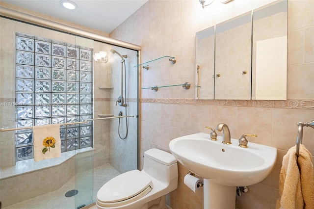 bathroom featuring sink, a shower with door, tile walls, and toilet