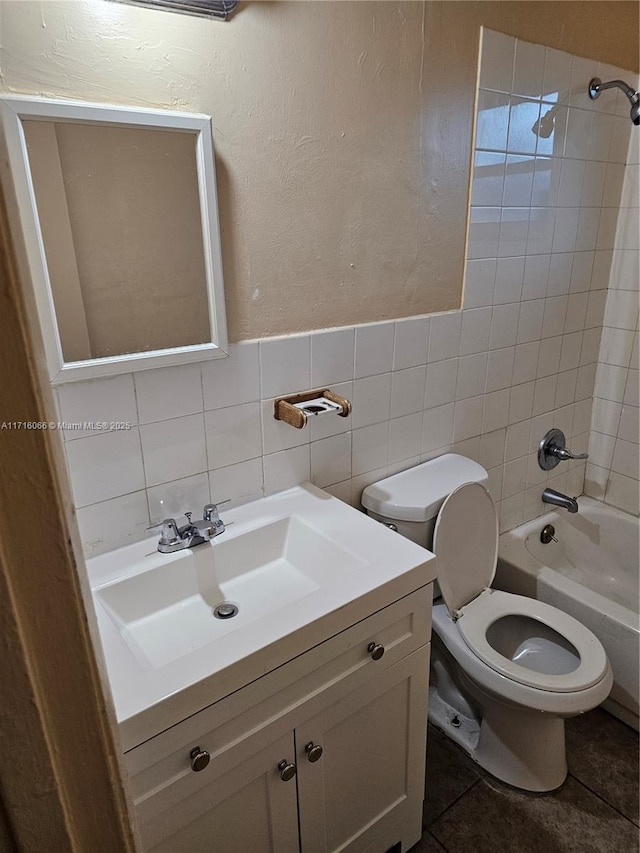 full bathroom with tile patterned floors, toilet, vanity, tile walls, and tiled shower / bath