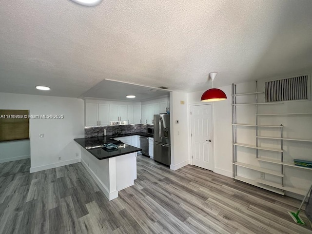 kitchen with decorative light fixtures, backsplash, kitchen peninsula, stainless steel appliances, and white cabinets