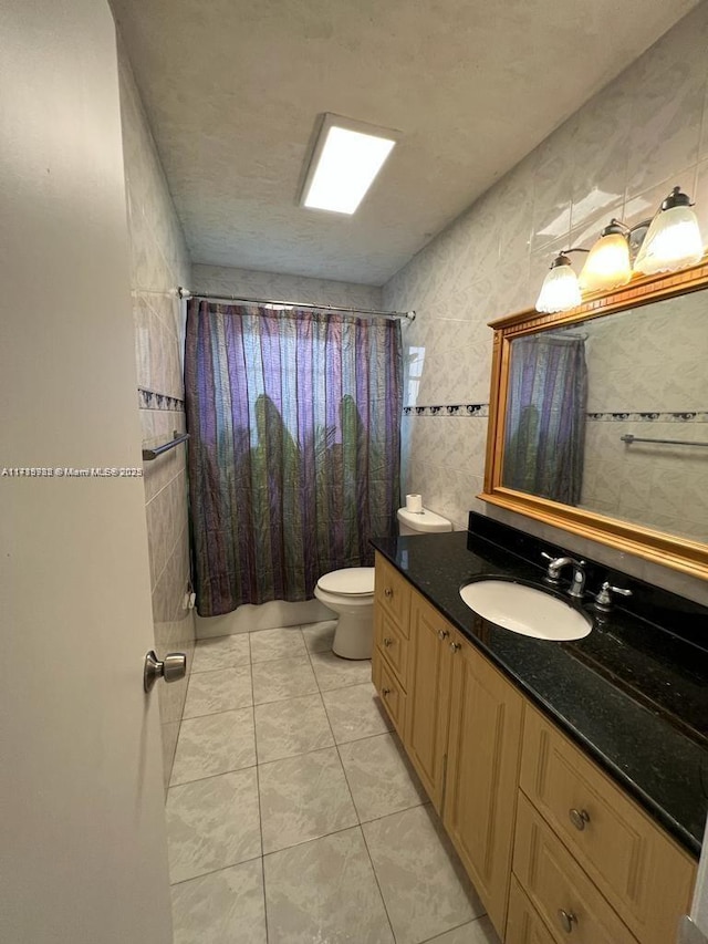 bathroom with a textured ceiling, tile patterned floors, vanity, tile walls, and toilet