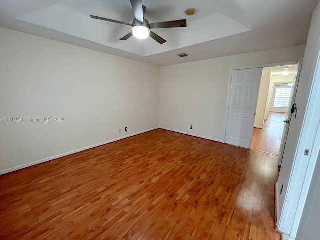 empty room with hardwood / wood-style floors, a raised ceiling, and ceiling fan