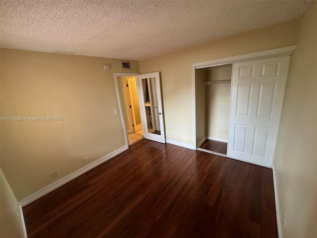 unfurnished bedroom featuring a textured ceiling, dark hardwood / wood-style floors, and a closet