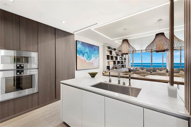 kitchen featuring sink, white cabinetry, dark brown cabinets, a water view, and stainless steel double oven