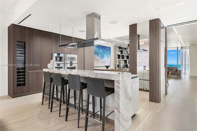 kitchen with wood walls, a kitchen bar, a large island, dark brown cabinetry, and light stone counters