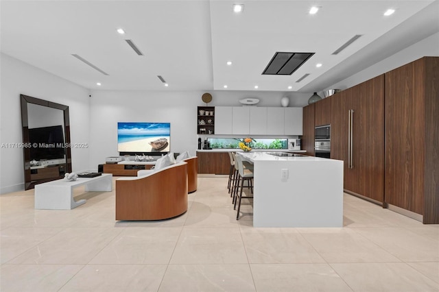 kitchen with stainless steel oven, a center island, light tile patterned floors, a kitchen bar, and white cabinets