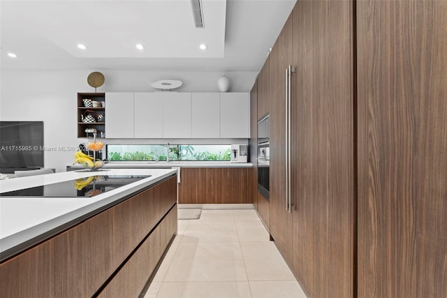 kitchen with high end fridge, black electric cooktop, light tile patterned floors, white cabinets, and oven