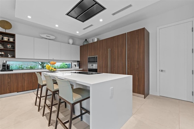 kitchen with white cabinets, black electric stovetop, built in microwave, a kitchen island, and a breakfast bar area