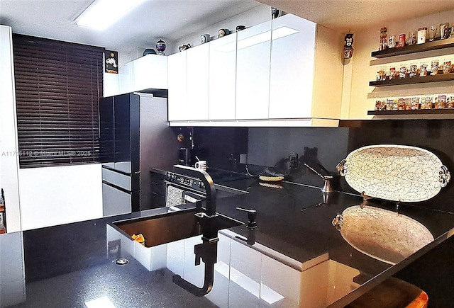 kitchen featuring white cabinets, decorative backsplash, stainless steel fridge, and sink