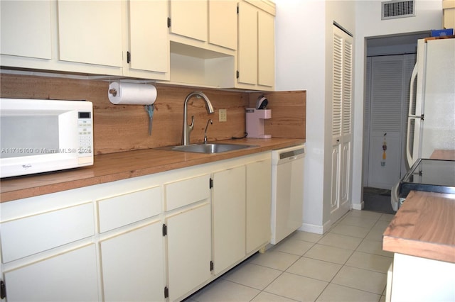 kitchen featuring decorative backsplash, white appliances, sink, light tile patterned floors, and cream cabinets